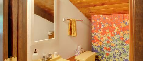 Un baño con techo de madera, un lavamanos amarillo, un inodoro y una cortina de ducha colorida.