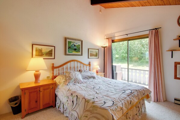 Un dormitorio con una cama, dos lámparas de noche, una mesita de madera, un cesto de basura y una ventana con cortinas.