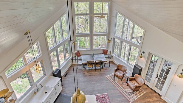 A spacious room with large windows, a wooden ceiling, a dining table with chairs, a sofa, and a fireplace. - Enchanting Tryon Home w/ Hot Tub ~ 14 Mi to Tiec! (Tryon)