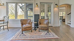 A spacious room with large windows, two leather chairs, a small table, and a patterned rug. - Enchanting Tryon Home w/ Hot Tub ~ 14 Mi to Tiec! (Tryon)