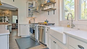 A modern kitchen with white cabinetry, stainless steel appliances, and a large window offering a view of trees. - Enchanting Tryon Home w/ Hot Tub ~ 14 Mi to Tiec! (Tryon)