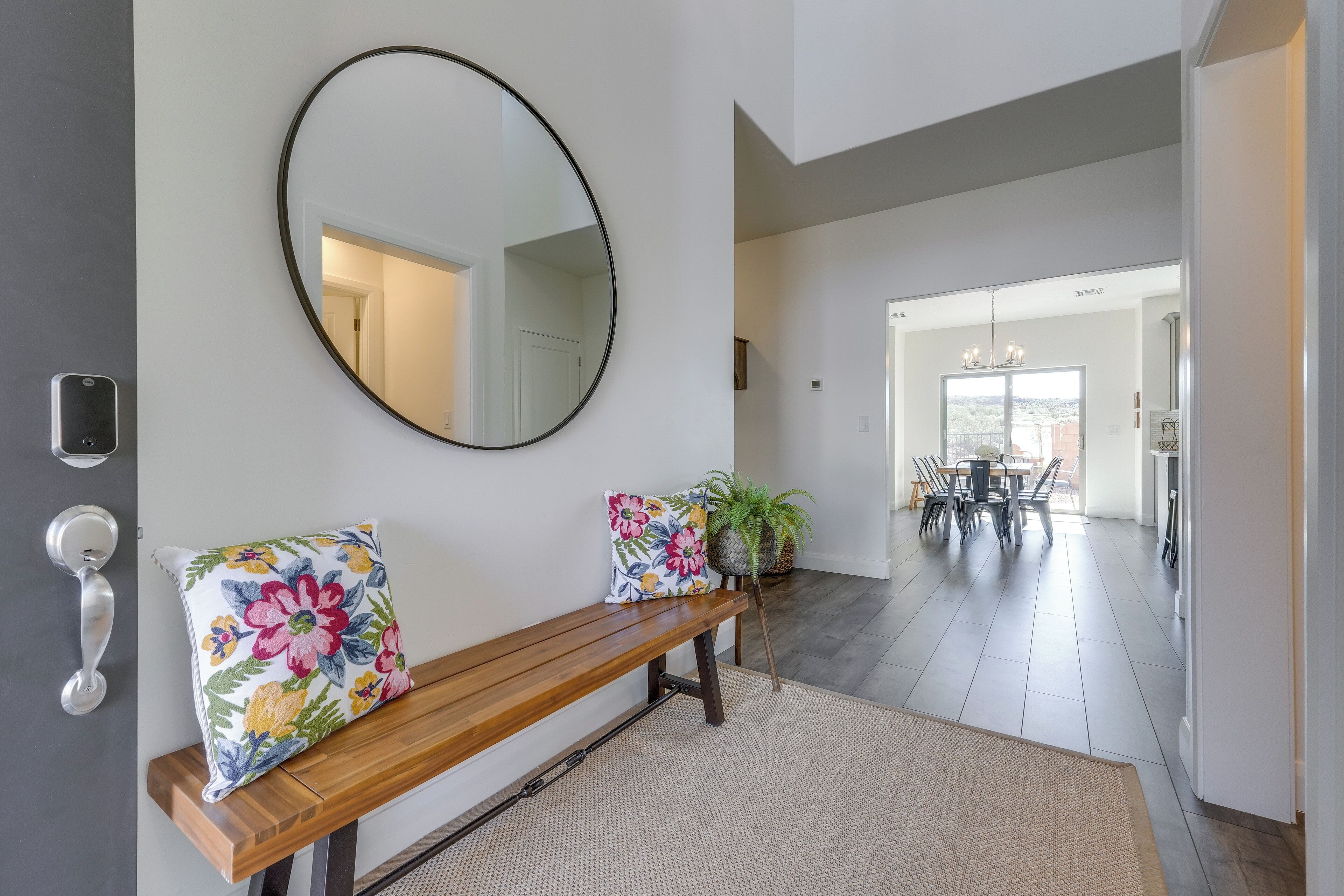 A hallway with a wooden bench, a round mirror, and a potted plant.