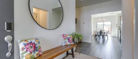 A hallway with a wooden bench, a round mirror, and a potted plant.