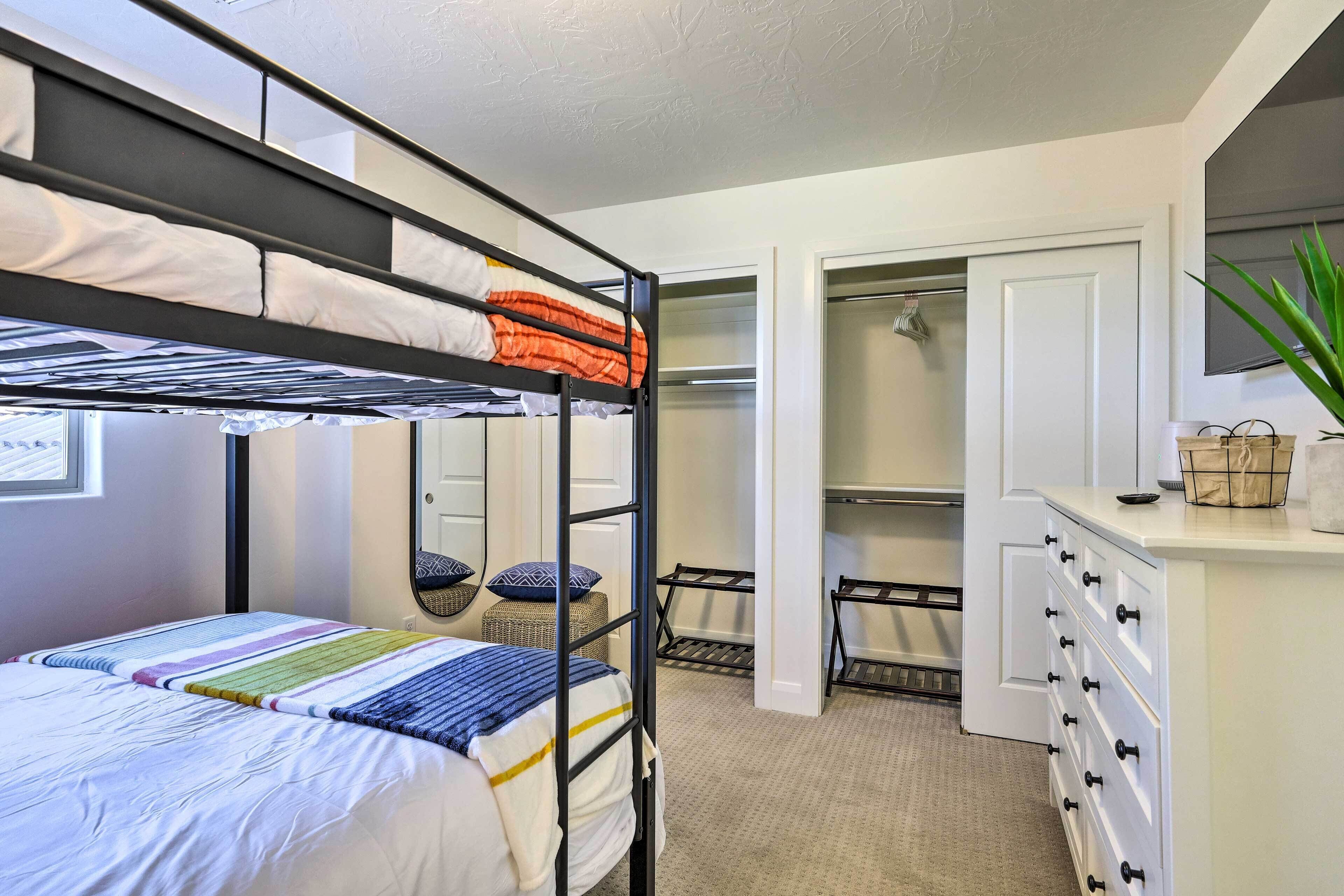 A bunk bed with a colorful blanket, a white dresser with drawers, a mirror, and a plant.