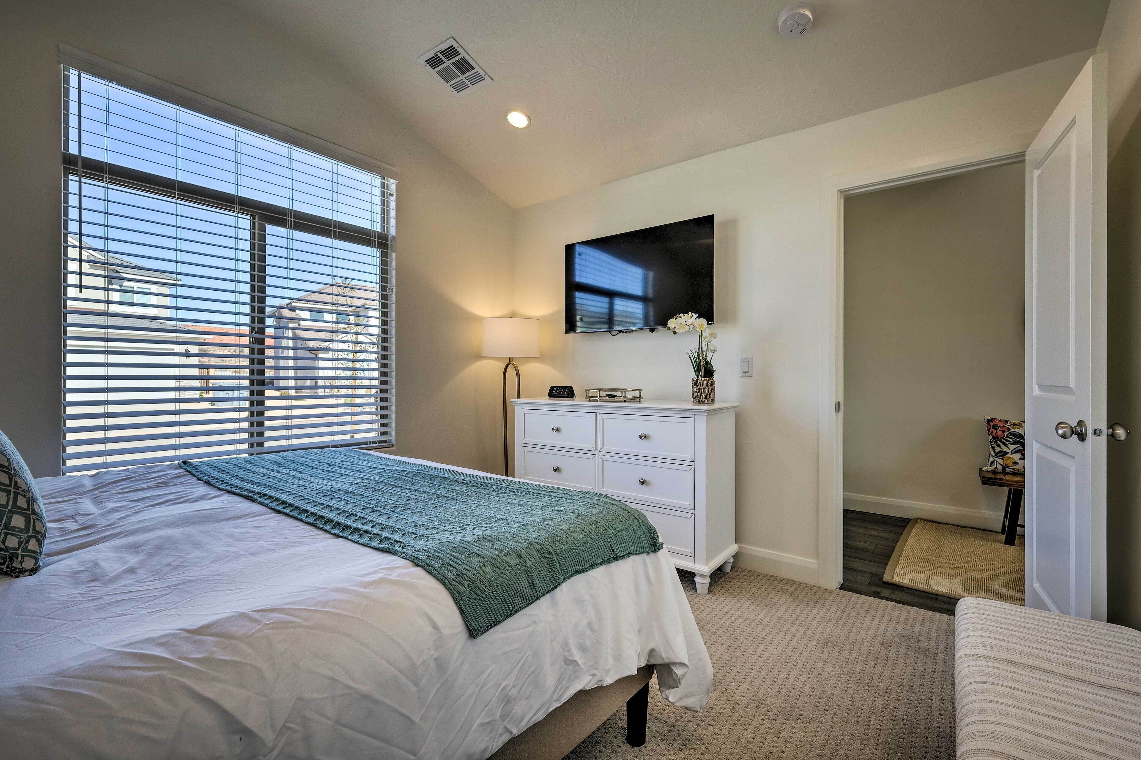 A bedroom with a bed, a dresser, a television, and a window with blinds.
