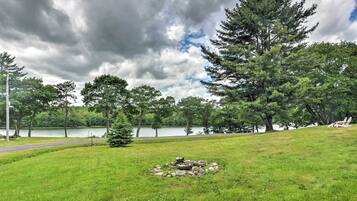 A grassy area with a fire pit, trees, and a lake in the background.