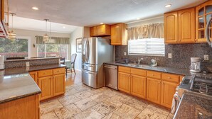 Una cocina con armarios de madera, encimeras de granito, electrodomésticos de acero inoxidable y una ventana con cortinas.