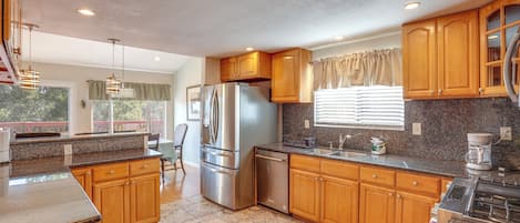Una cocina con armarios de madera, encimeras de granito, electrodomésticos de acero inoxidable y una ventana con cortinas.