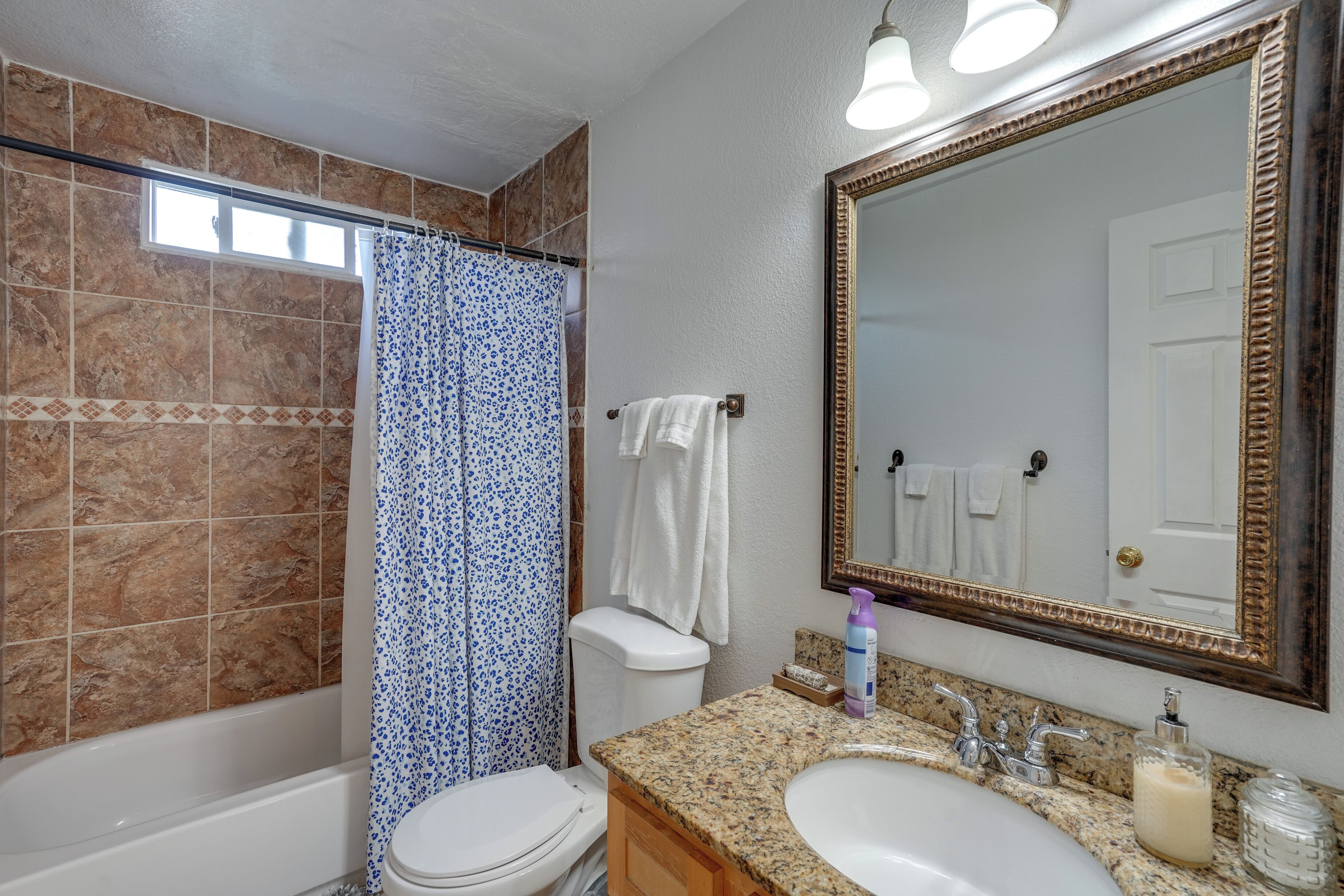 Un baño con bañera, ducha con cortina azul estampada, inodoro, lavamanos con espejo y toallero.