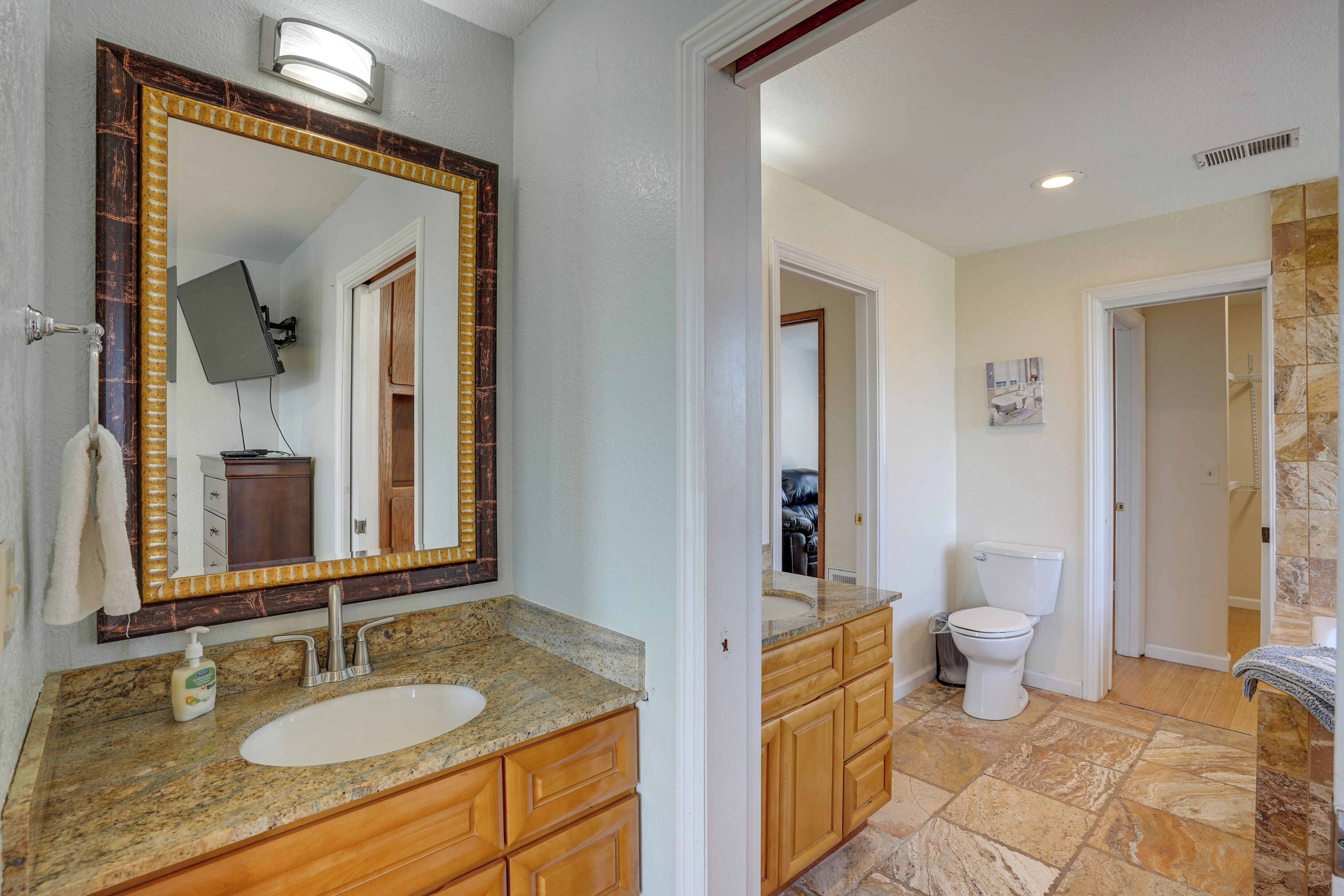 A bathroom with a large mirror, granite countertop, wooden cabinets, and a white toilet.