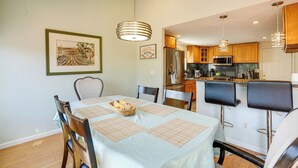 Un comedor con una mesa dispuesta para cuatro, una cocina al fondo y un cuadro en la pared.