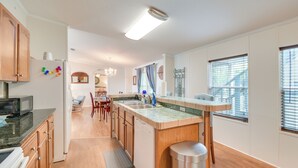 Una cocina moderna con armarios de madera, microondas integrado y un cubo de basura de acero inoxidable.
