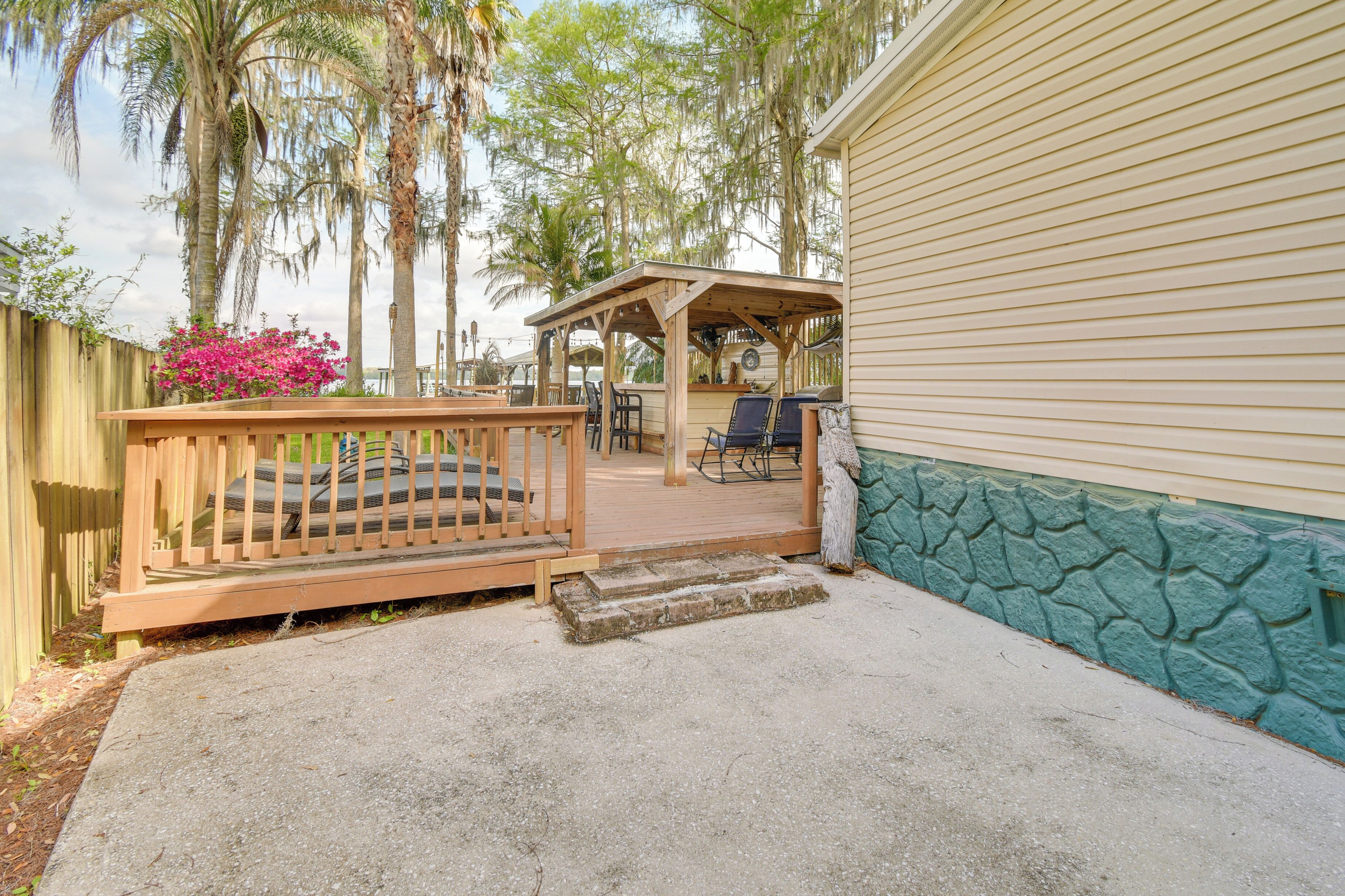 A covered patio with a wooden deck, a concrete pathway, and a stone wall.