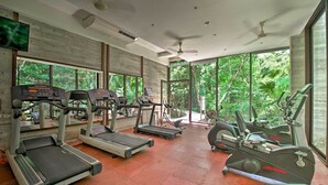 A gym with treadmills, elliptical machines, and a stationary bike, large windows with a view of greenery, and ceiling fans. - Luxe Tao Riviera Resort Condo w/ Beach & Golfing! (Akumal)