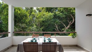 A balcony with a table set for four, surrounded by chairs, overlooking a lush green garden. - Luxe Tao Riviera Resort Condo w/ Beach & Golfing! (Akumal)