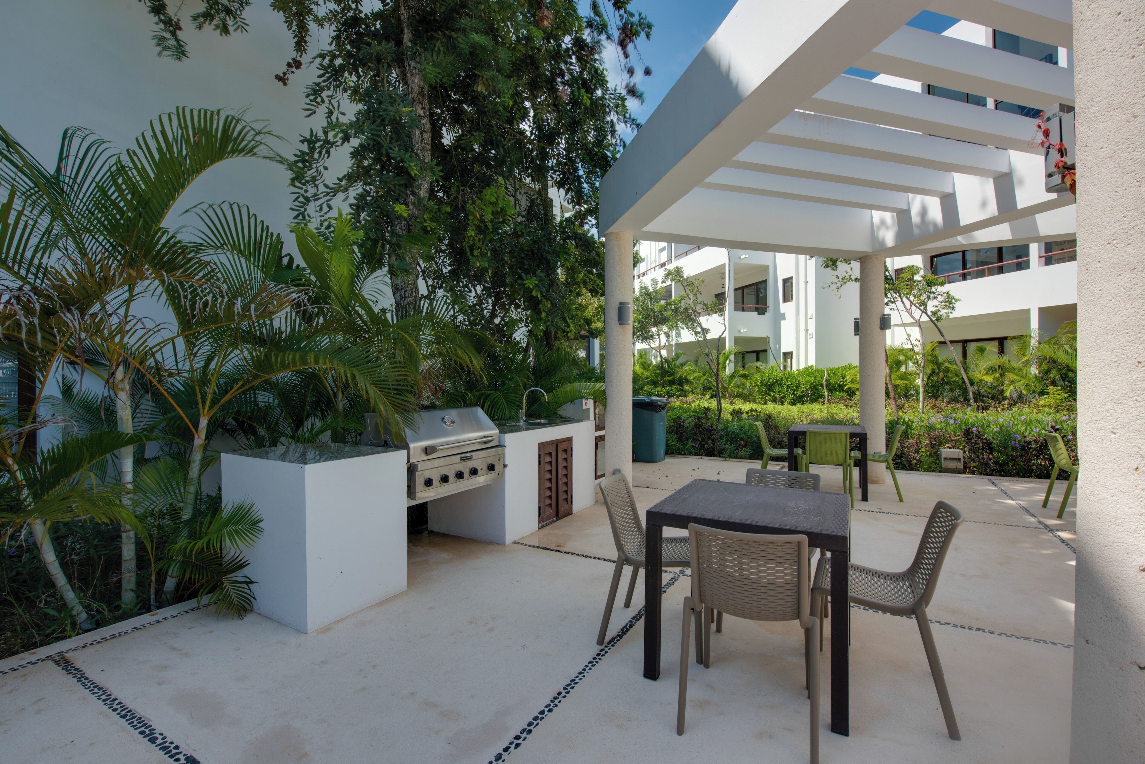 An outdoor patio with a grill, seating area, and lush greenery.