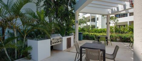An outdoor patio with a grill, seating area, and lush greenery.