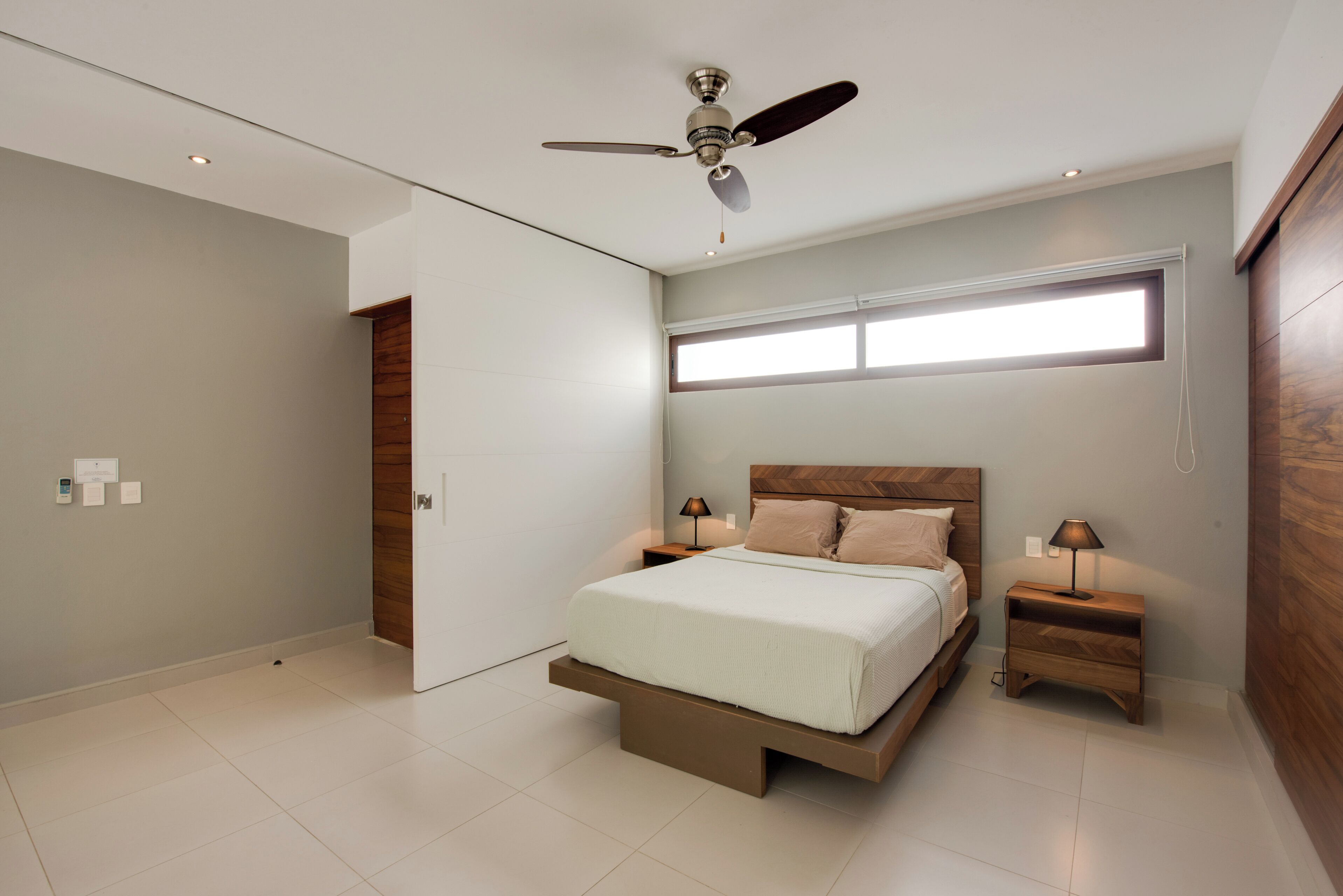 A modern bedroom with a bed, nightstands, a ceiling fan, and a window.
