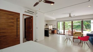 A spacious room with a bed, a dining area, and a kitchen. There are ceiling fans and a large window providing natural light. - Luxe Tao Riviera Resort Condo w/ Beach & Golfing! (Akumal)