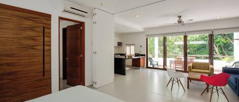 Una habitación amplia con cama, comedor y cocina. Cuenta con ventiladores de techo y un ventanal grande que proporciona luz natural.