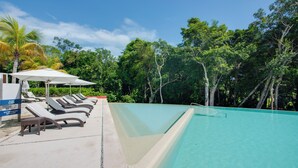 A swimming pool with lounge chairs and umbrellas, surrounded by lush greenery. - Luxe Tao Riviera Resort Condo w/ Beach & Golfing! (Akumal)