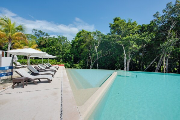 A swimming pool with lounge chairs and umbrellas, surrounded by lush greenery.