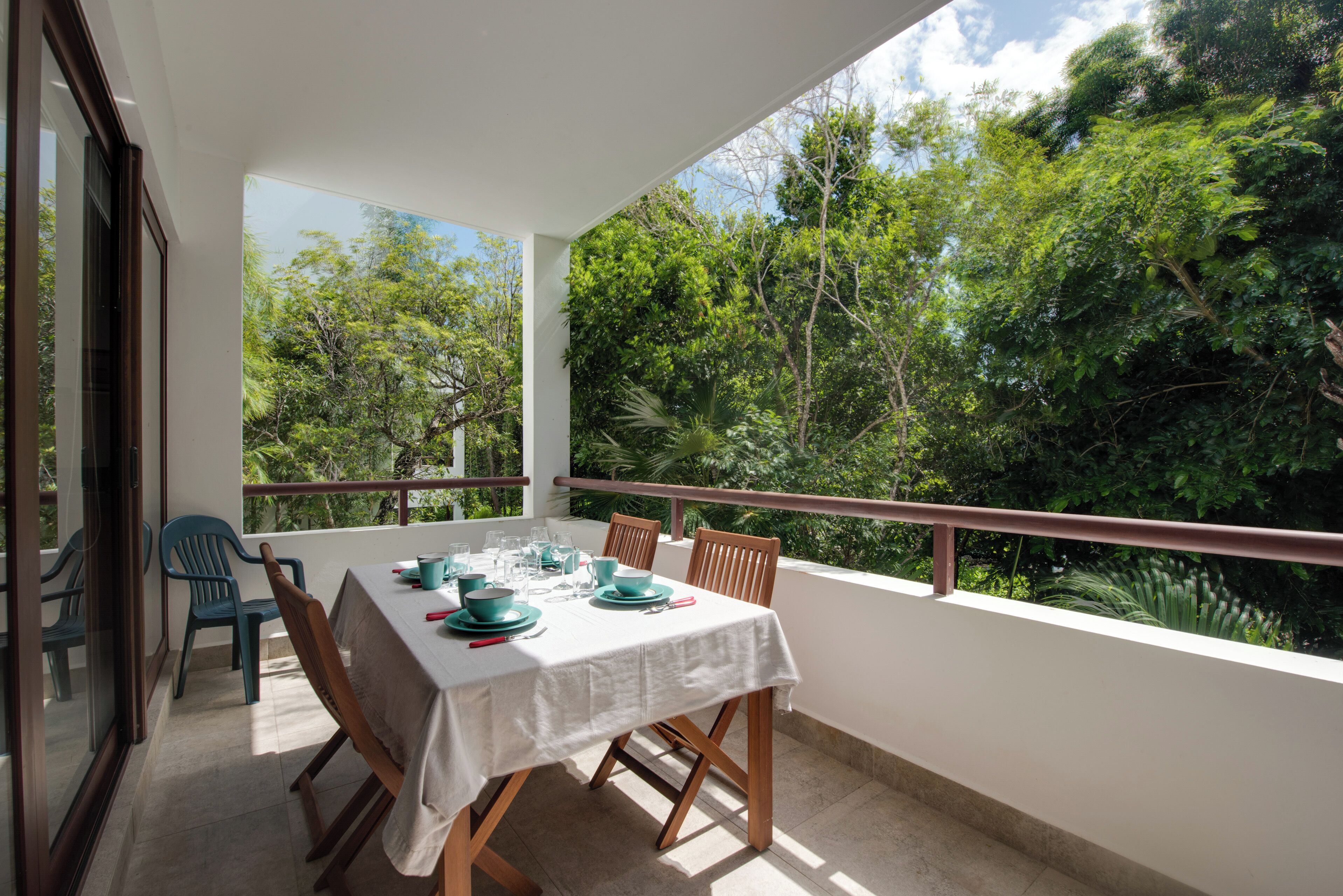 Un balcon avec une table dressée pour le dîner, donnant sur une forêt verdoyante et luxuriante.