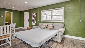 A room with a bed, a gray couch, a white chair, a window, and a door.