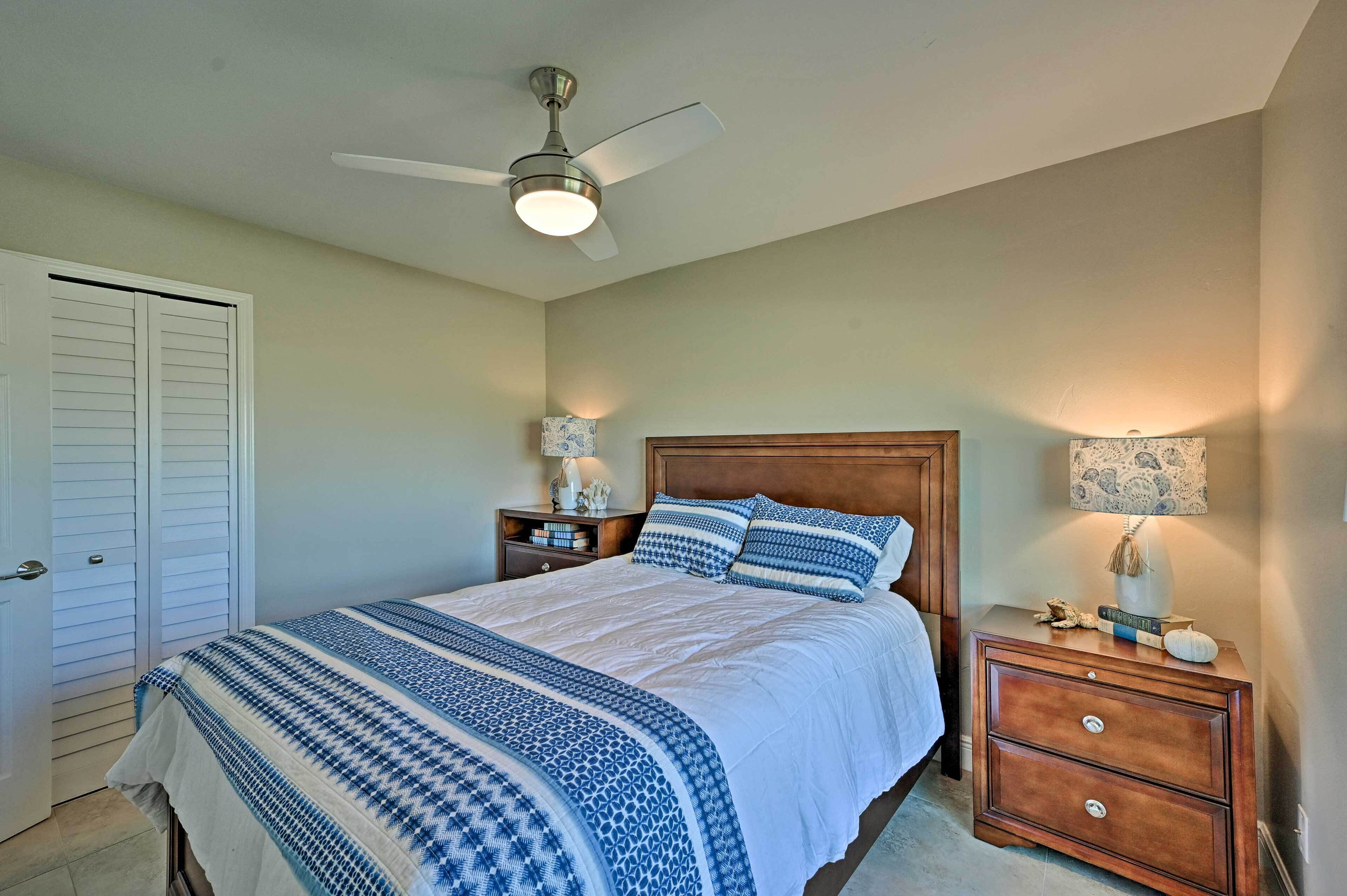 A bedroom with a bed, two nightstands, a ceiling fan, and a door.