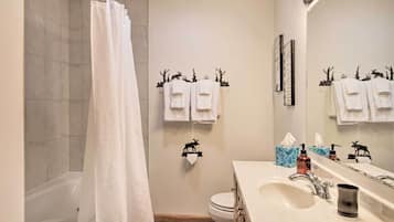 A bathroom with a bathtub, toilet, and sink. There are towels hanging on a rack and a mirror above the sink.