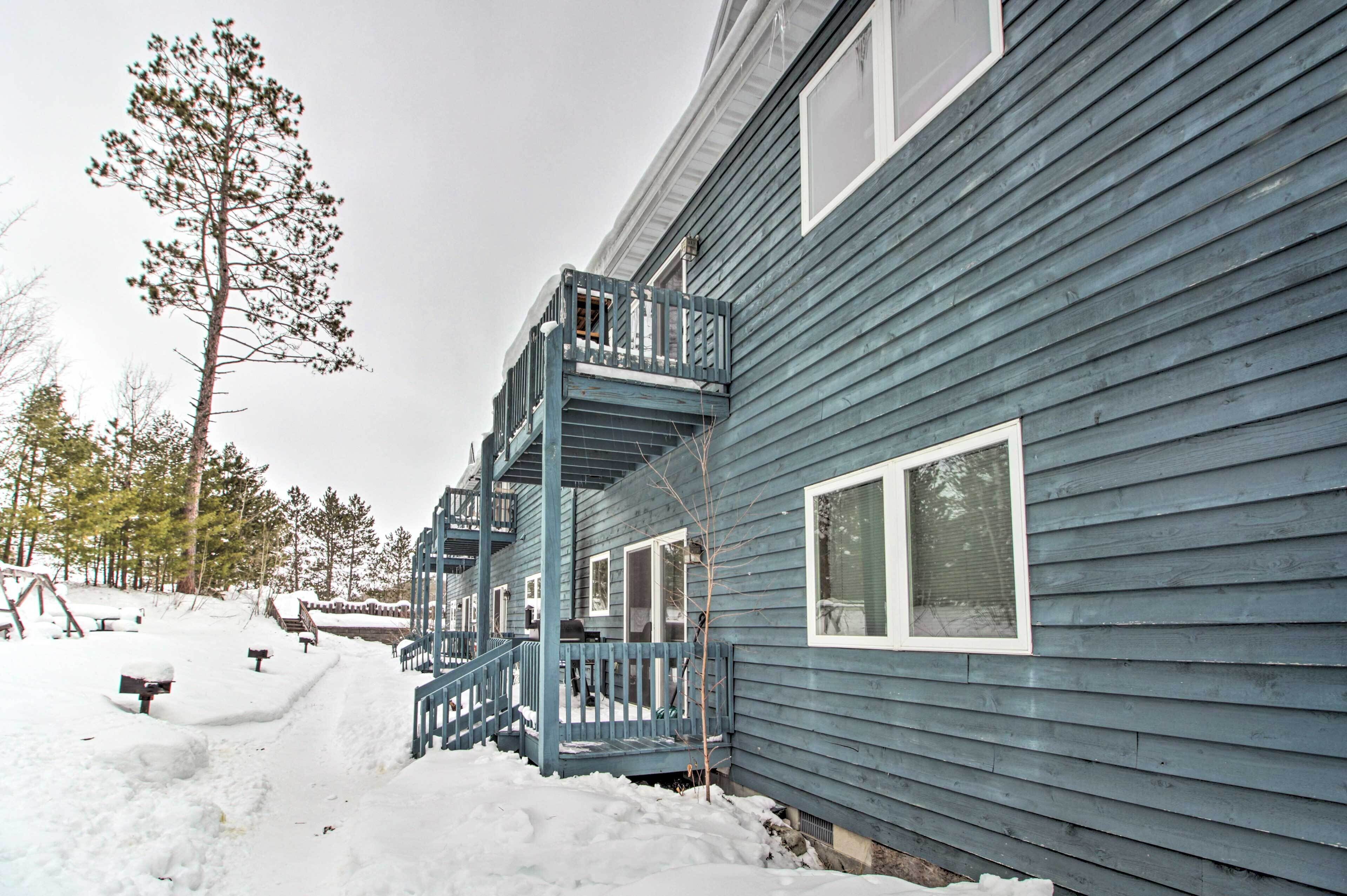 Un edificio de dos pisos con fachada azul, un balcón en el segundo piso y terreno cubierto de nieve.