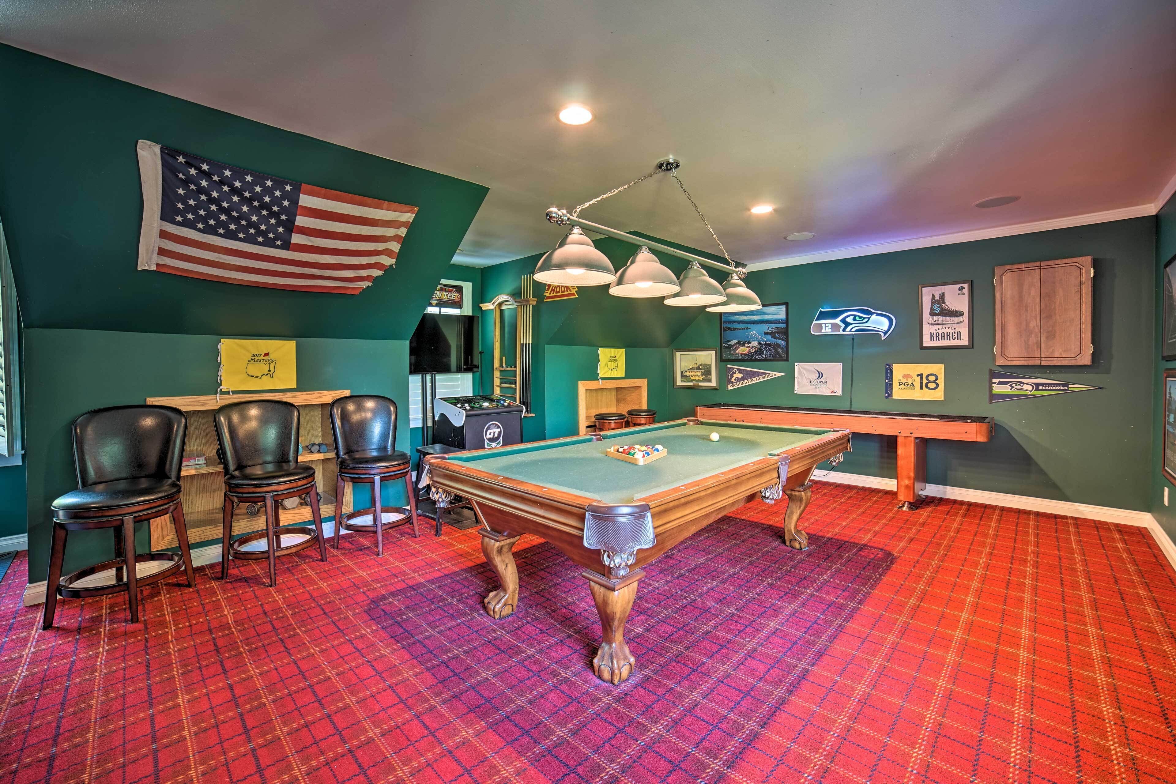 A pool table with a red plaid carpet, a pool cue, and three chairs.