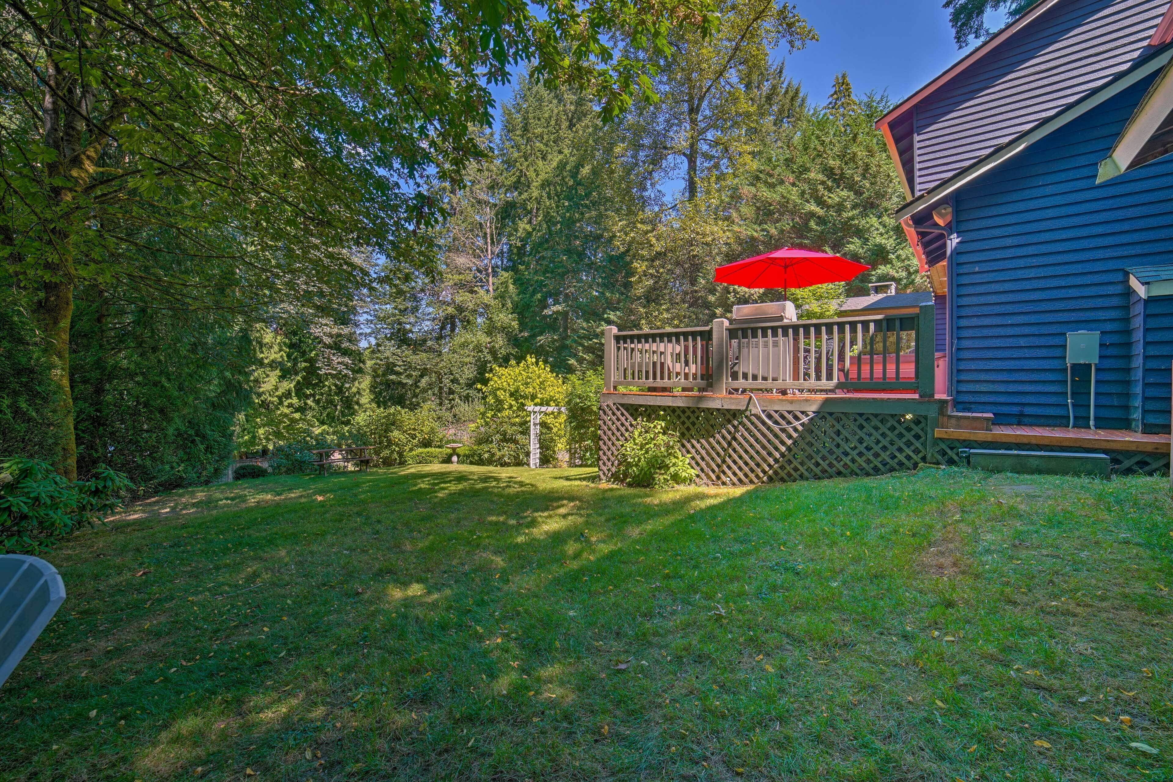 A backyard with a wooden deck, a red umbrella, and a blue house.