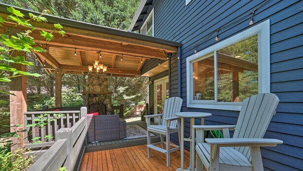Une terrasse en bois agrémentée de chaises Adirondack et d’une cheminée en pierre, le tout entouré d’une clôture en bois et d’une pergola illuminée de guirlandes lumineuses.