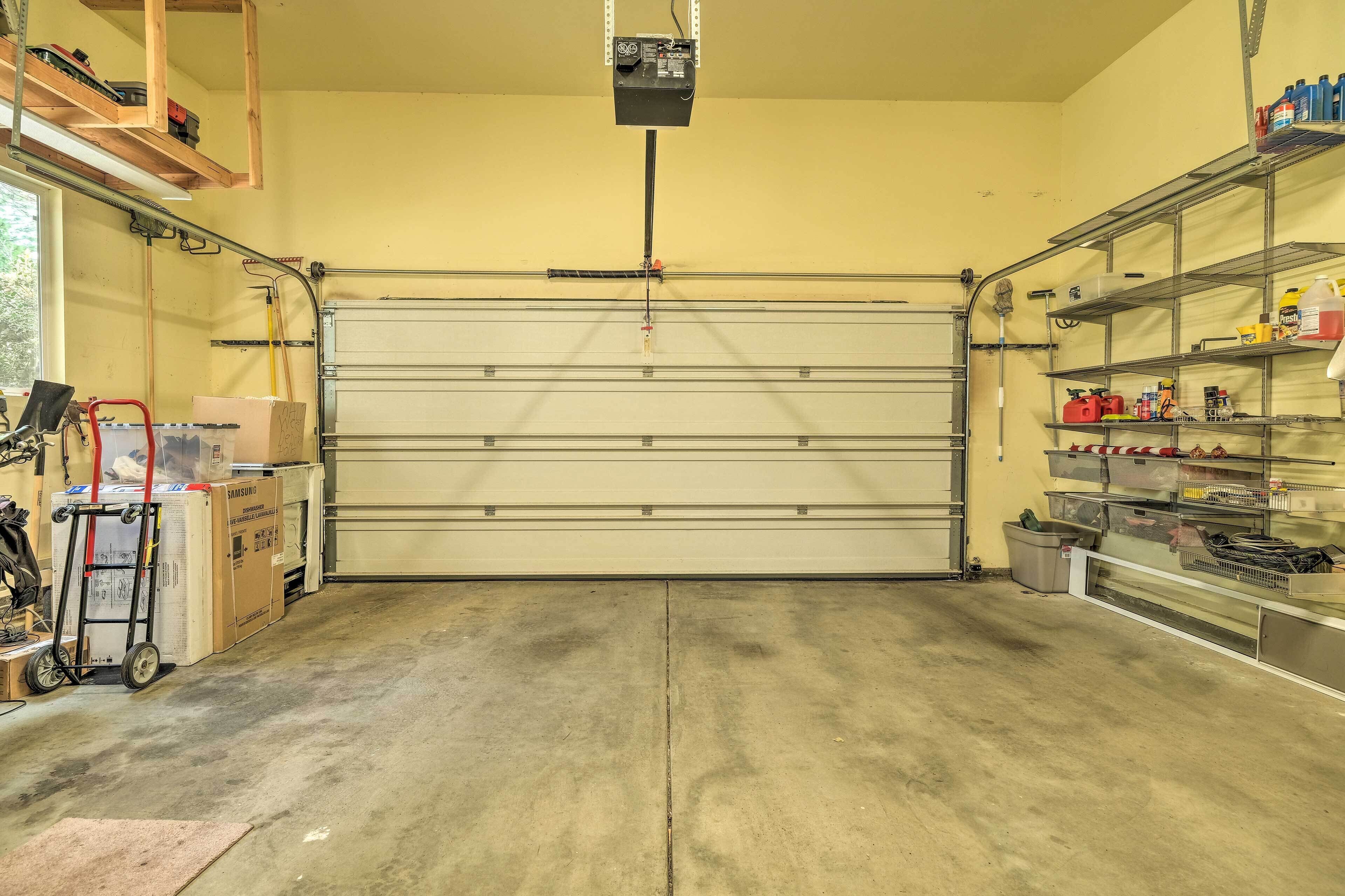 Un garage avec une grande porte, des étagères remplies de divers objets et un chariot contenant des cartons.