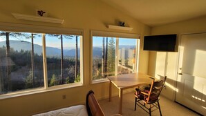 A bedroom with a large window, a bed, a wooden table, a chair, and a television. - Near Hiking: Home w/ Deck in Twain Harte! (Mi-Wuk Village)