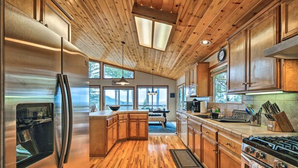 A modern kitchen with wooden cabinets, stainless steel appliances, and large windows offering views of the outdoors. - Near Hiking: Home w/ Deck in Twain Harte! (Mi-Wuk Village)