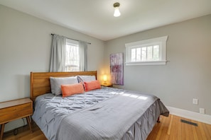 A bedroom with a wooden bed, a nightstand, a window with curtains, and a wall-mounted artwork. - Charming Tacoma Vacation Home w/ Fenced Yard (Tacoma)
