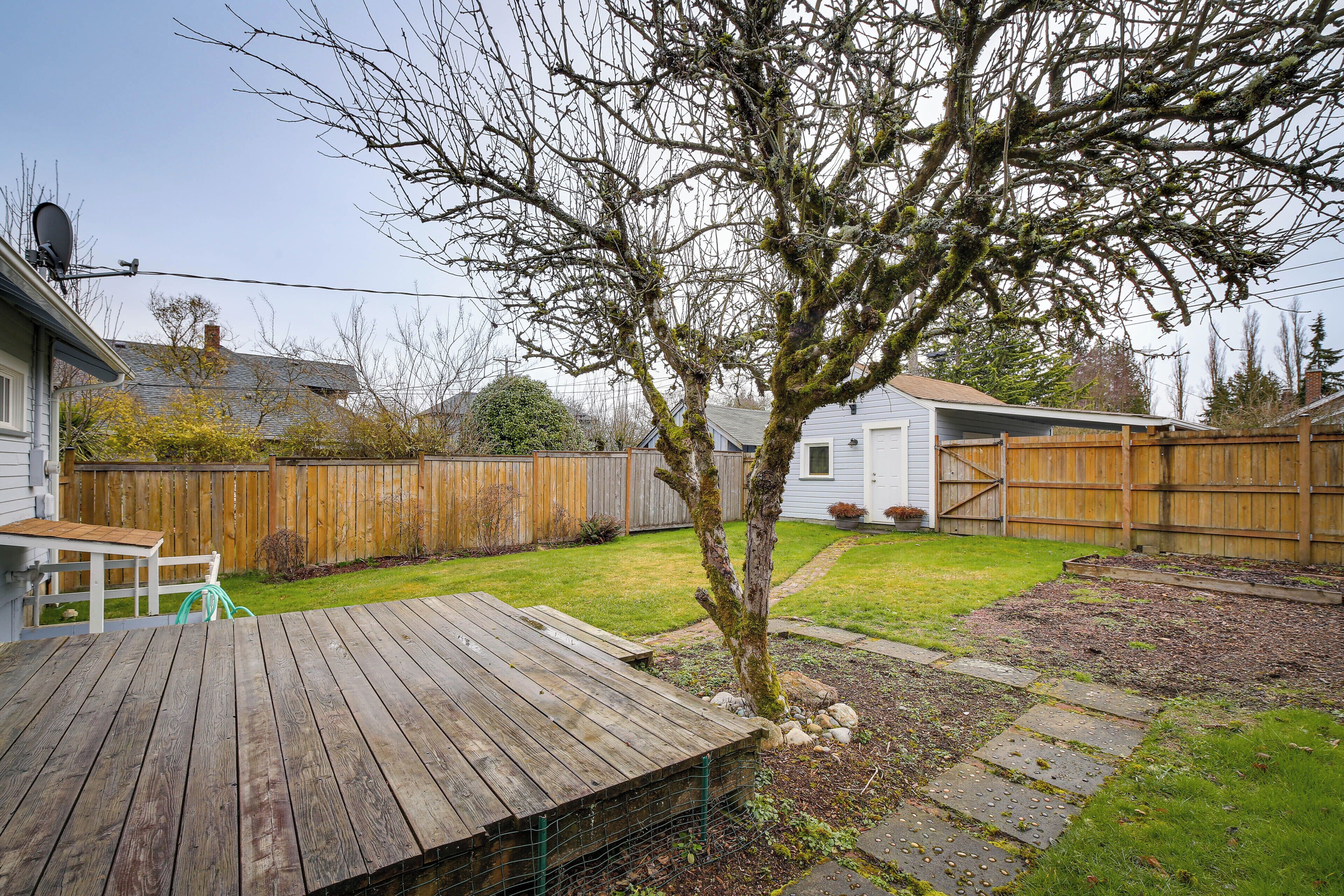 Eine Holzterrasse mit einem kleinen Tisch und Stühlen, umgeben von einem eingezäunten Garten mit Baum und Rasenfläche.