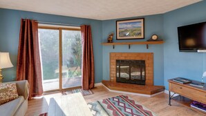 A living room with a fireplace, a sofa, a TV, and a large window with curtains. - Charming Anchorage Home w/ Grill + Deck! (Anchorage)