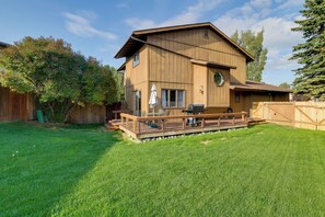Una casa de madera de dos pisos con un balcón, zona de barbacoa y patio trasero cercado.