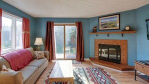 A living room with a sofa, a fireplace, a table, and a view through a glass door. - Charming Anchorage Home w/ Grill + Deck! (Anchorage)