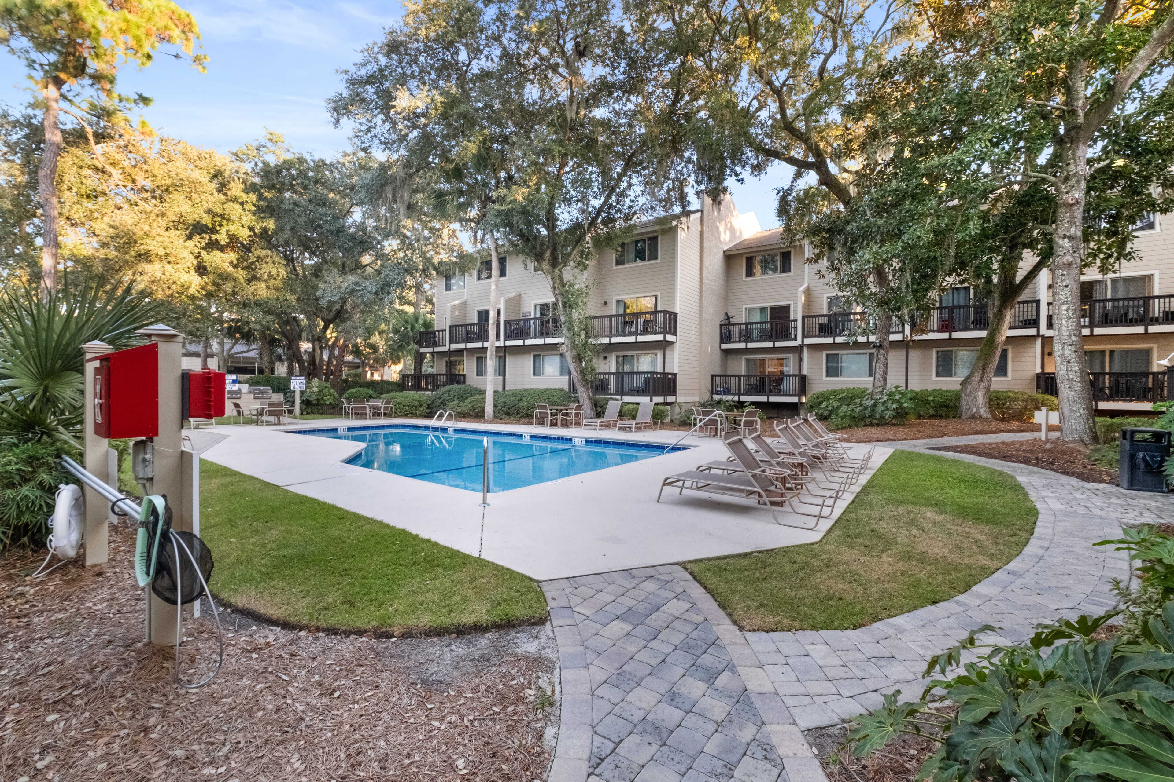 A pool area with lounge chairs, a red utility box, and a building with balconies.