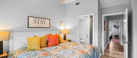 Un dormitorio con una colcha estampada con motivos florales, un ventilador de techo y un cartel que dice 'STAY'.