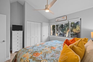 A bedroom with a bed, a ceiling fan, a dresser, a television, and a window with a view of palm trees. - Family-friendly Hilton Head Villa: Walk to Beach (Hilton Head Island)