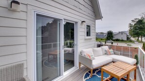 A covered outdoor seating area with a white sofa, a wooden table, and a glass door leading to a patio. - Riverfront Sheboygan Townhome w/ Grill! (Sheboygan)