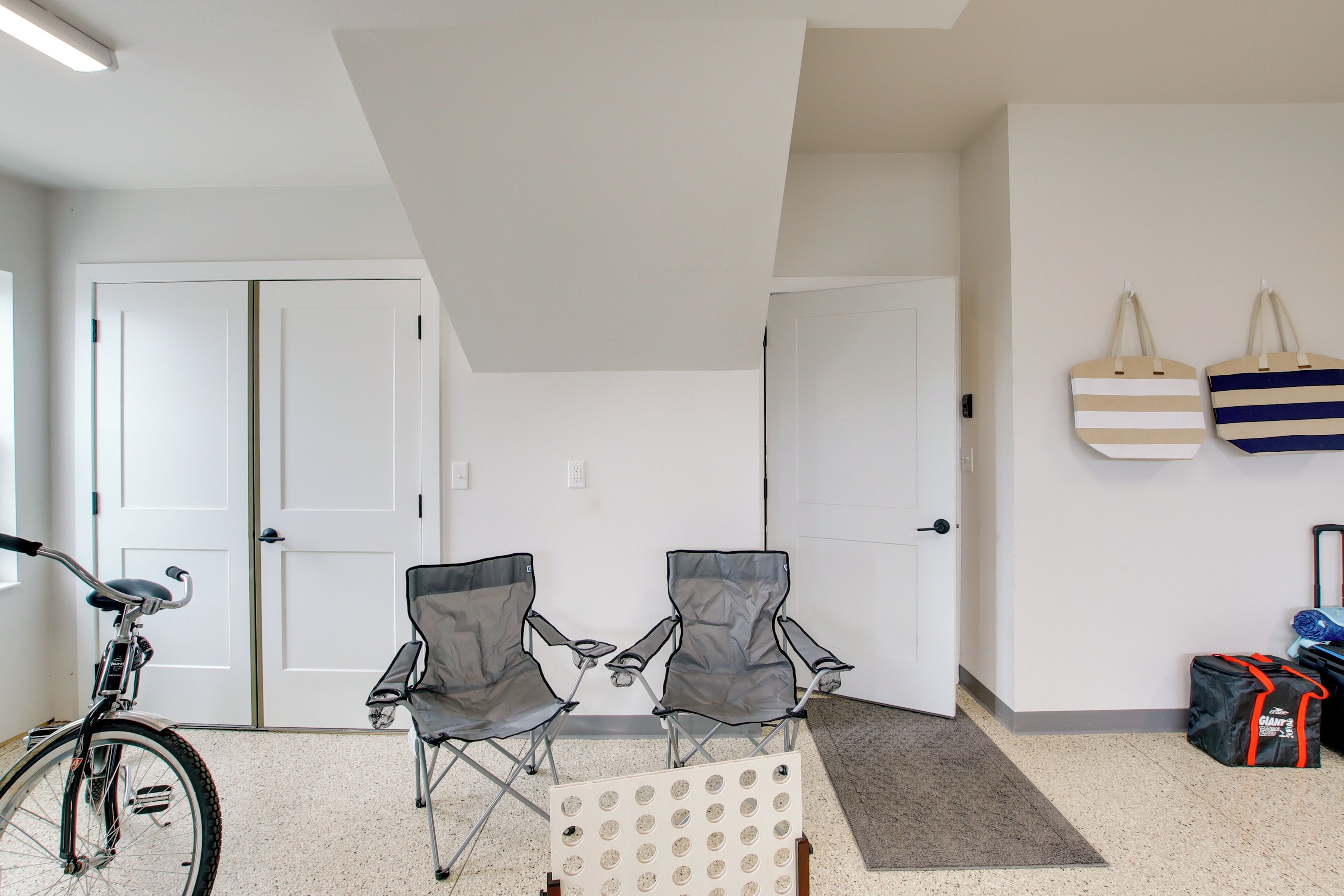 A room with two folding chairs, a bicycle, and a wall-mounted bag rack with bags.