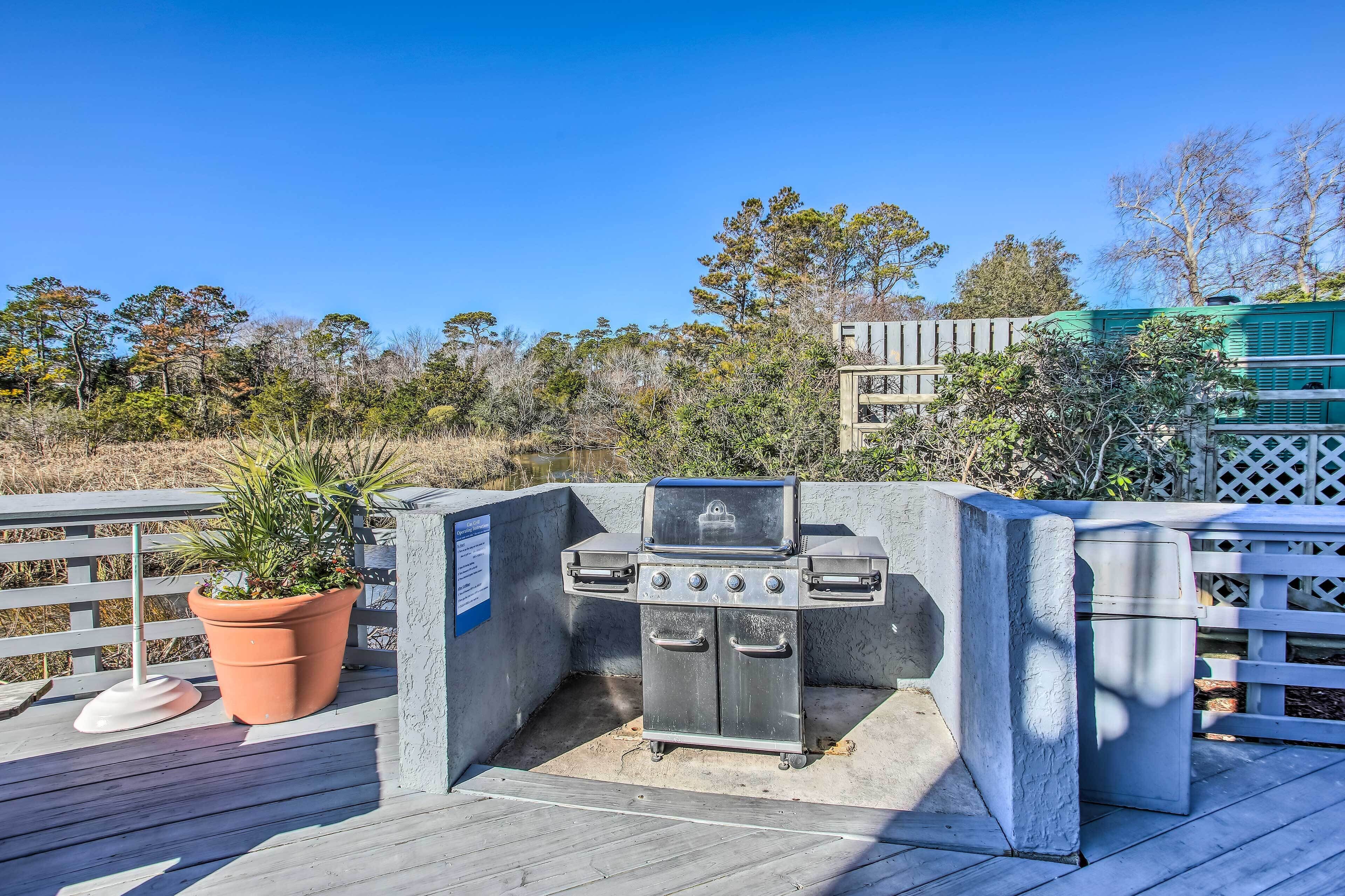 An outdoor grill area with a wooden deck, surrounded by a white fence and trees.