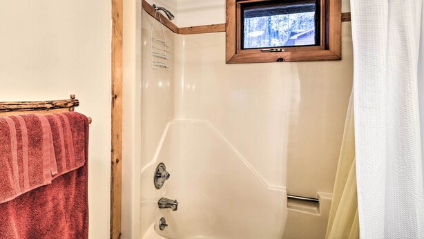 A bathroom with a shower, a window with a view of a snowy landscape, and a towel rack with a red towel.