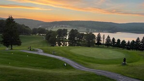 A golf course with a lake, trees, and a sunset.